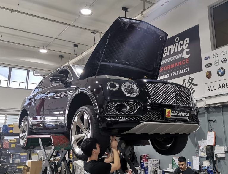 Bentley car raised on a lift with mechanics working on repairs in a modern automotive service workshop.